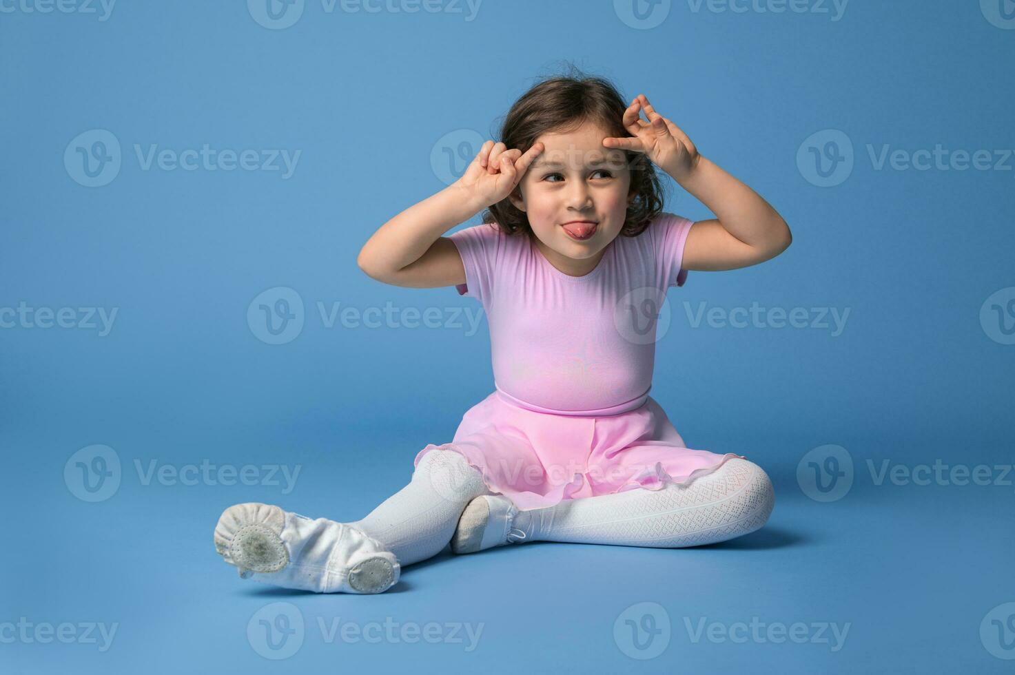 isolé portrait plus de bleu Contexte de un adorable préscolaire fille ballerine grimaçant et montrant sa langue . photo