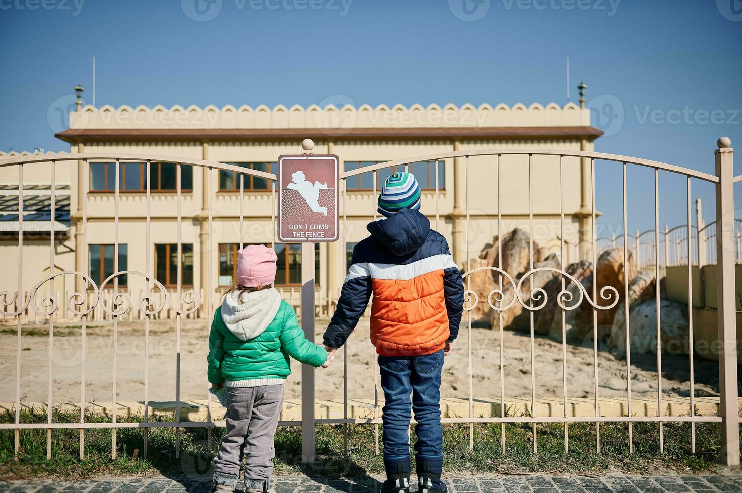 vue de le retour à une garçon en portant le sien sœurs main et permanent dans une de face de zoo cage photo