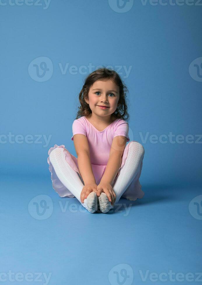 portrait sur une bleu Contexte de une mignonne ballerine dans une rose robe élongation sa corps photo