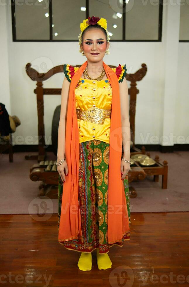 une traditionnel indonésien Danseur permanent dans une Jaune costume et un Orange écharpe pendaison vers le bas sa corps photo