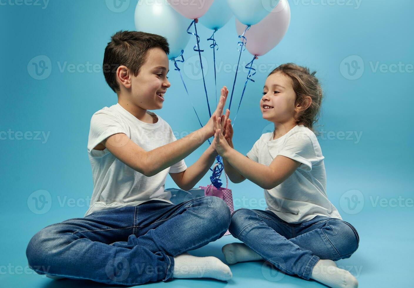 garçon et fille applaudir mains tandis que posant sur bleu Contexte avec des ballons derrière leur photo