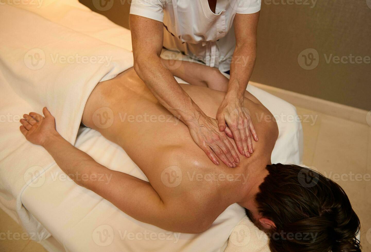 aérien vue de méconnaissable professionnel massage thérapeute masser retour muscles de une Jeune homme, relaxant, mensonge vers le bas sur massage table à luxe bien-être spa centre. alternative thérapie concept photo