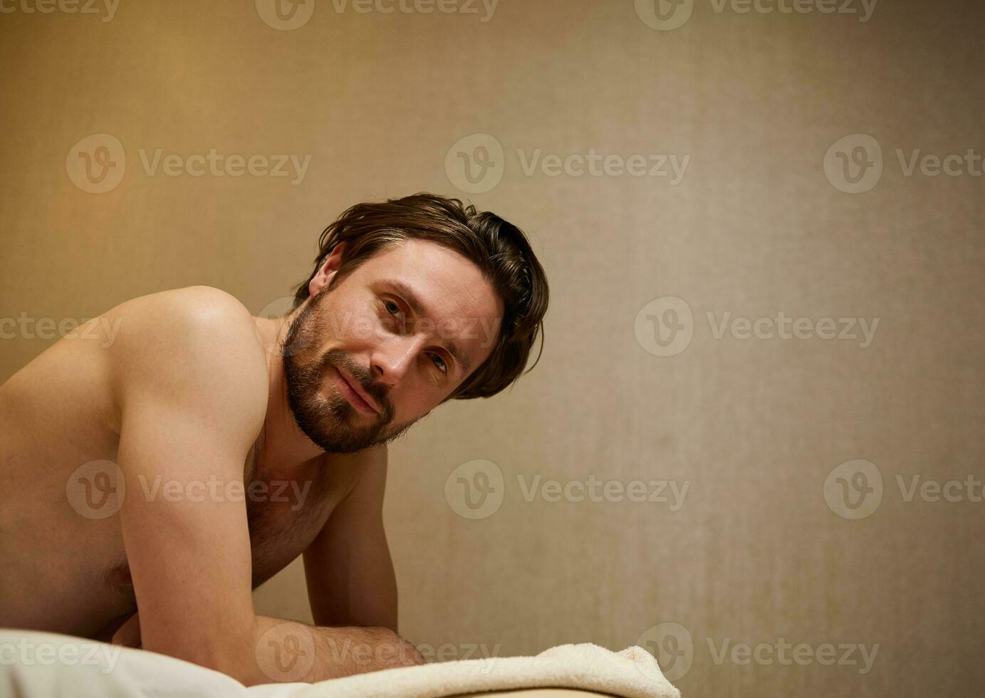 Beau milieu vieilli caucasien homme mensonge sur une massage tableau, sourit à la recherche à caméra, avoir prêt à recevoir professionnel corps massage thérapie à bien-être centre. ayurveda et corps se soucier concept photo