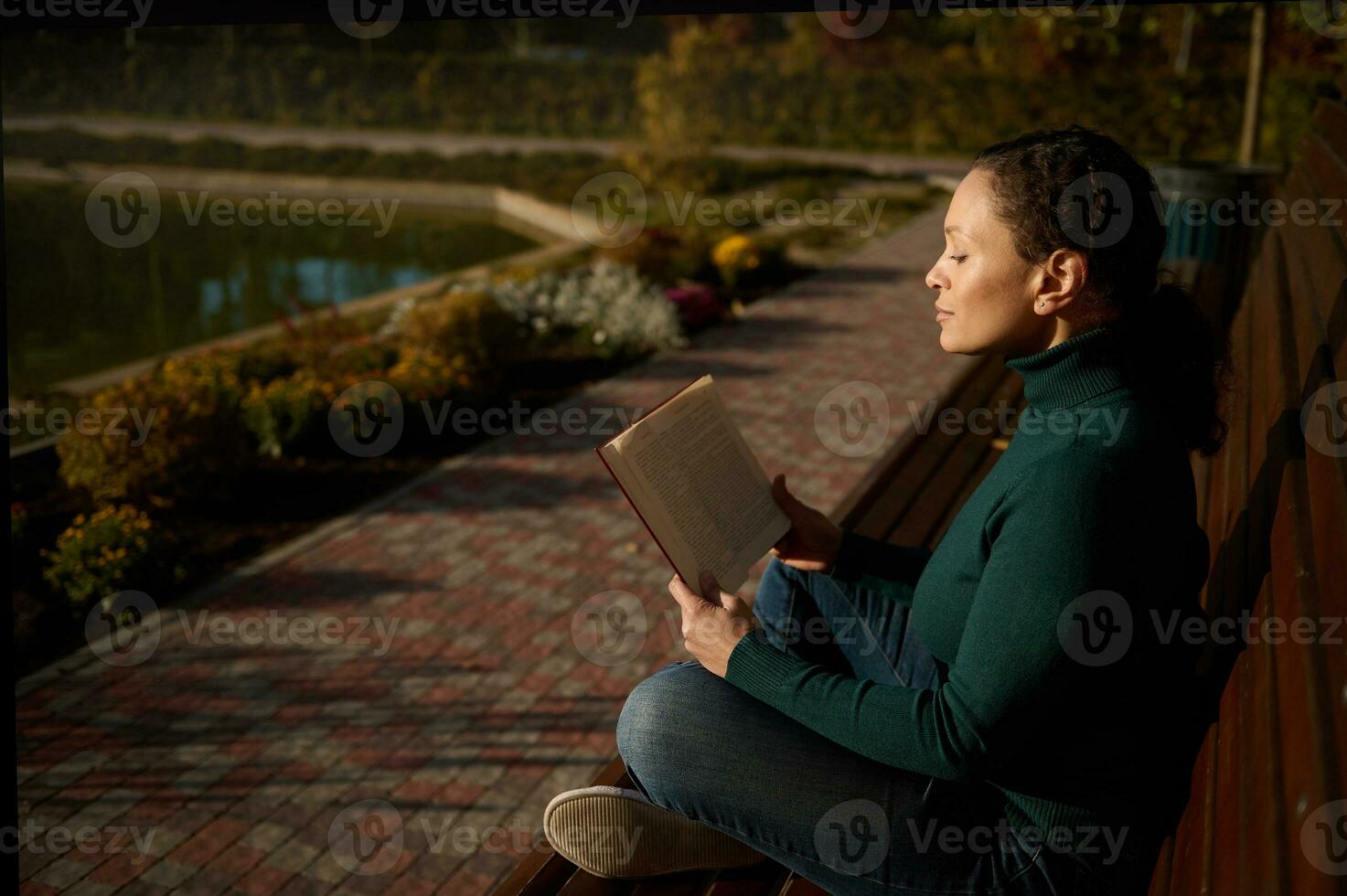 côté portrait de paisible jolie femme séance sur en bois banc dans parc, en train de lire livre, profiter chaud ensoleillé l'automne journée , une façon de le bousculer et agitation de ville, repos de numérique gadgets et travail photo