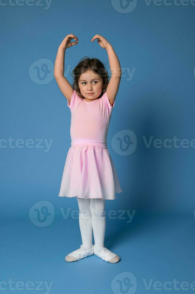 une gracieux peu ballerine performant pose dans ballet danse, permanent isolé plus de bleu Contexte photo