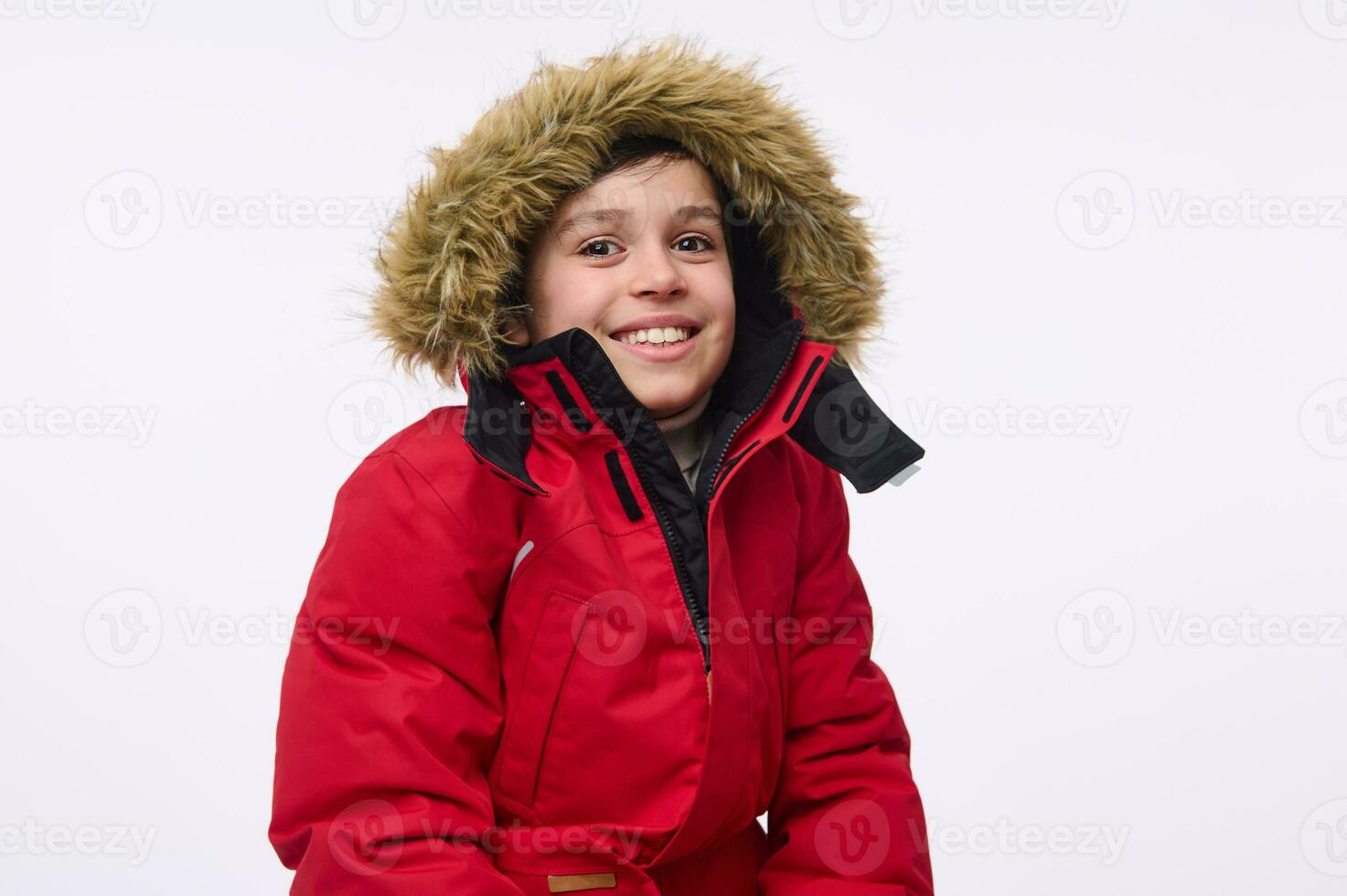 taille longueur portrait de Beau de bonne humeur préadolescent, école vieilli garçon portant brillant rouge vers le bas veste avec capot, souriant à pleines dents sourire à la recherche à caméra isolé sur blanc Contexte avec copie espace photo