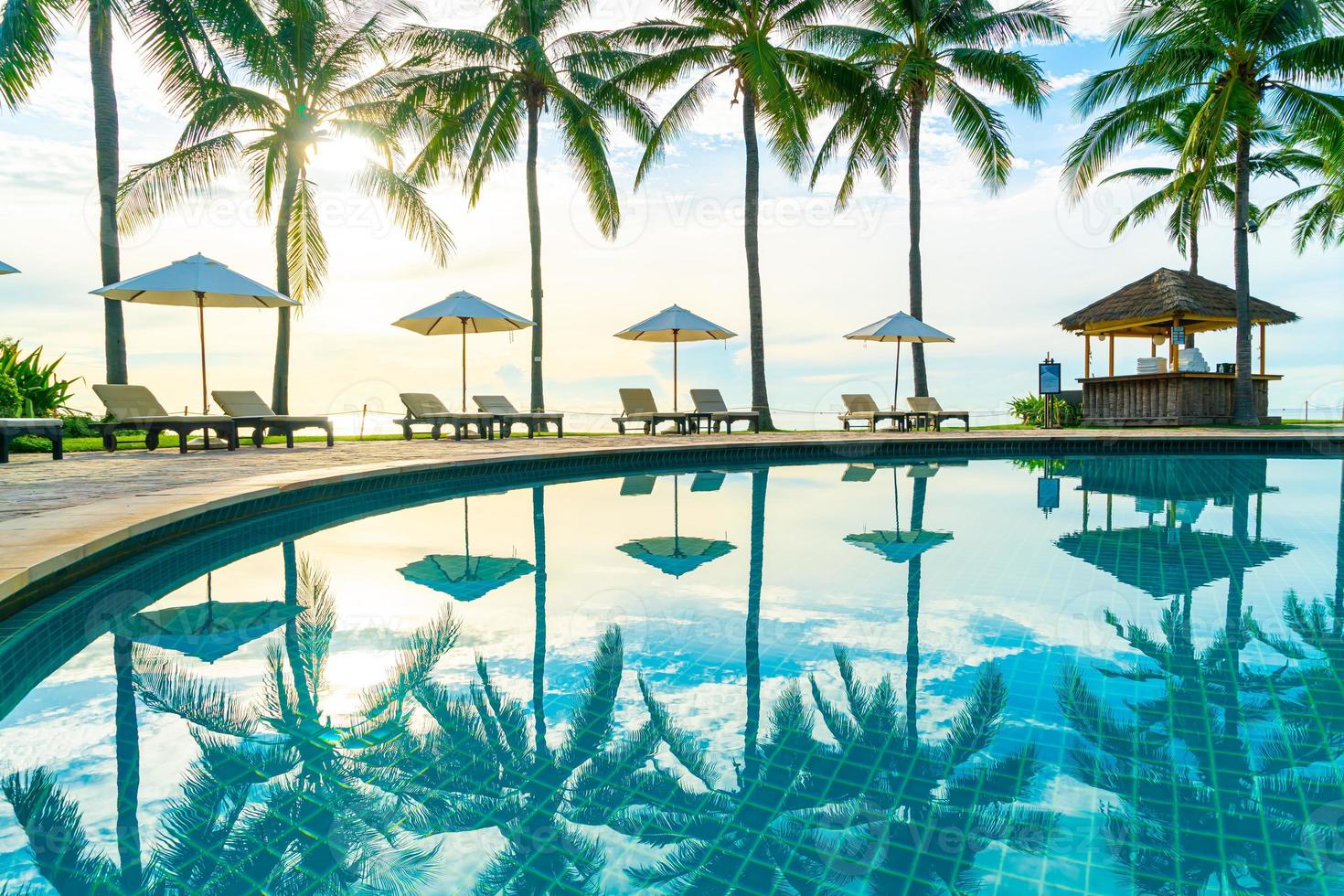 beau parasol et chaise de luxe autour de la piscine extérieure de l'hôtel et du complexe avec cocotier au coucher du soleil ou au lever du soleil photo