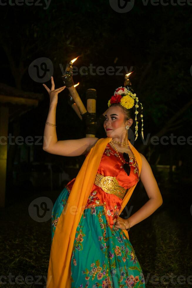 une traditionnel asiatique Danseur pose dans de face de une brûlant torche dans un Orange costume lequel est très magnifique photo
