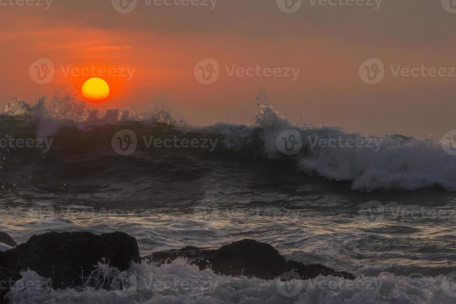 vagues éclaboussant les rochers au coucher du soleil photo