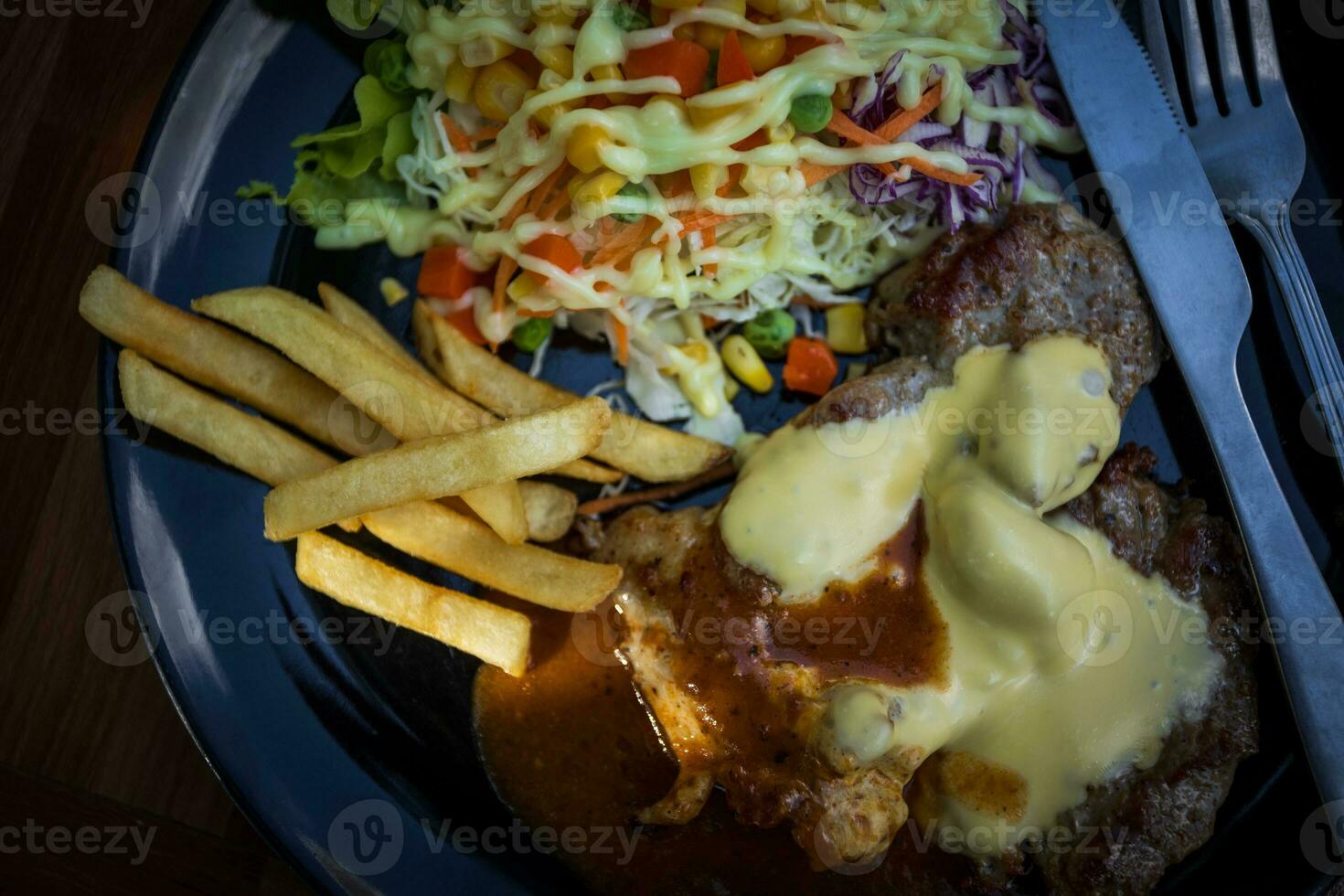 fromage porc steak sur une noir assiette avec légume salade photo