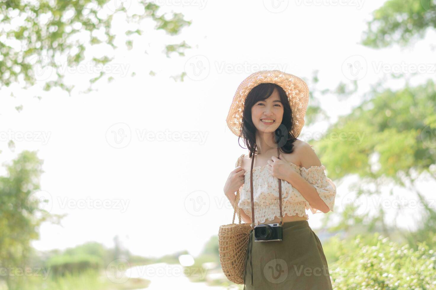 portrait de asiatique Jeune femme voyageur avec tissage chapeau et panier et une caméra sur vert Publique parc la nature Contexte. périple voyage mode de vie, monde Voyage explorateur ou Asie été tourisme concept. photo