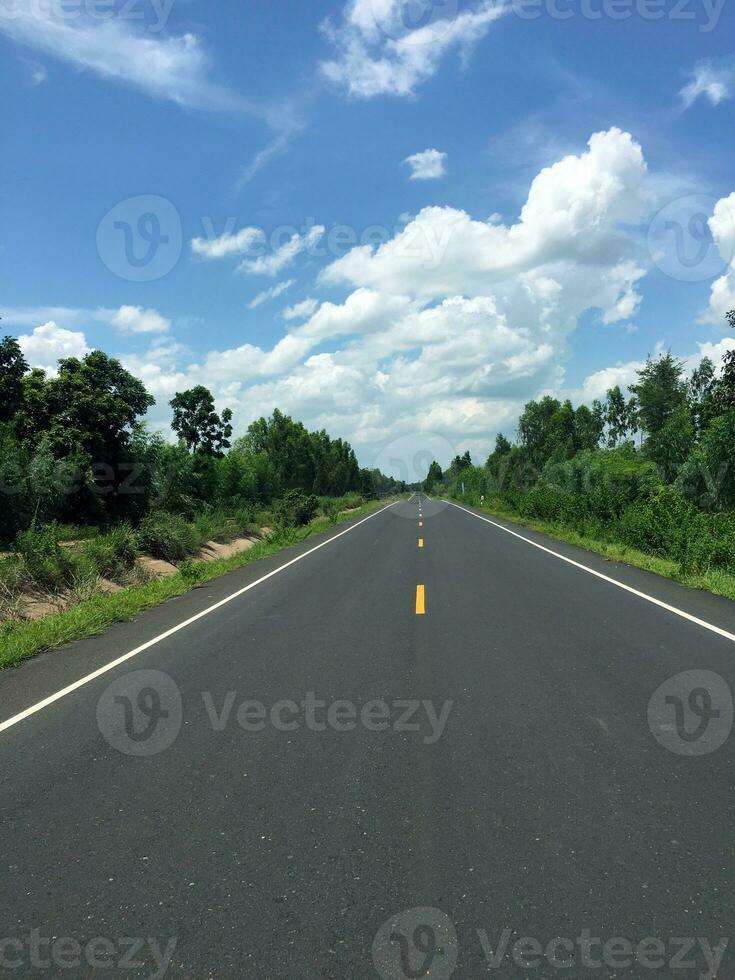 image de Nouveau pavé route dans le jour dans le campagne peint Jaune partage ligne avec des arbres, herbe le long de le route, ciel avec blanc des nuages photo