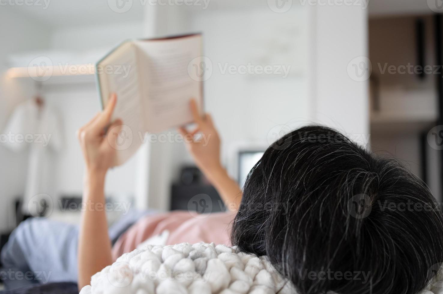 Femme d'âge moyen allongée sur le lit et lisant un livre à l'hôtel pendant les vacances photo