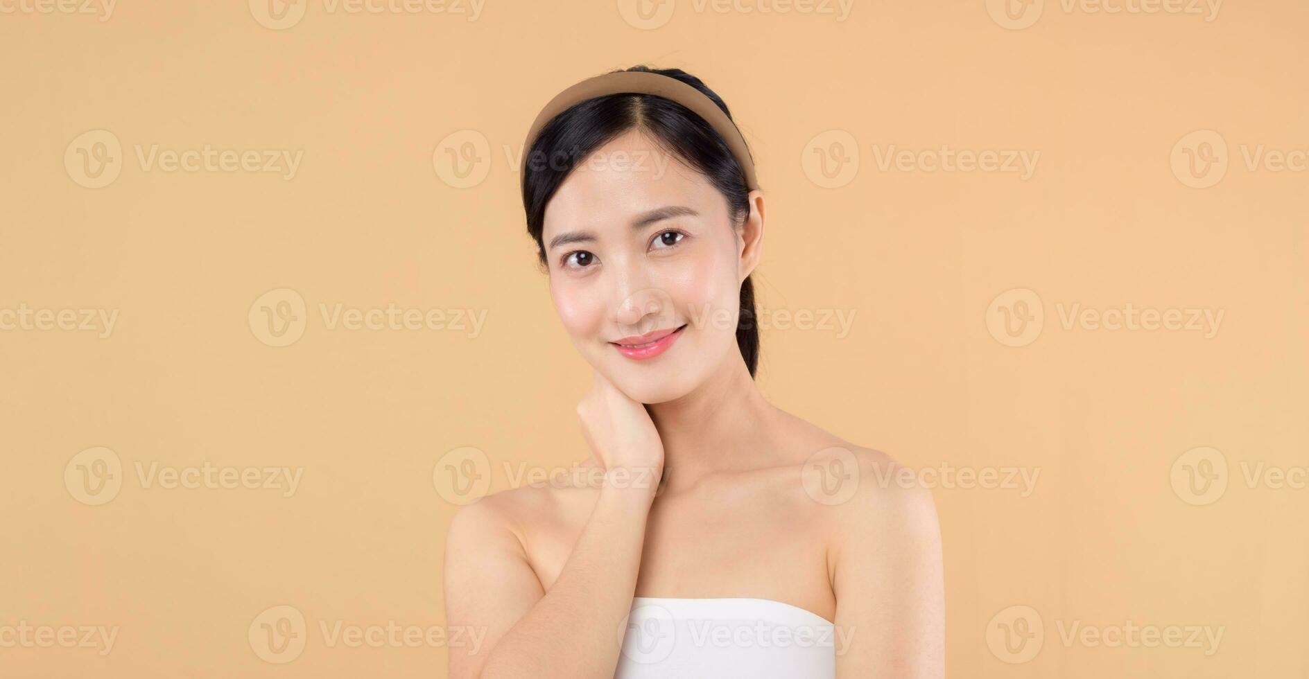 magnifique fille asiatique modèle émouvant Frais embrasé hydraté faciale peau sur beige Contexte fermer. beauté visage Jeune femme avec Naturel maquillage et en bonne santé peau portrait. peau se soucier concept photo