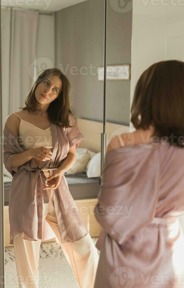 content Matin. attrayant Jeune femme à la recherche dans miroir à sa appartement - réveiller en haut et Nouveau journée photo