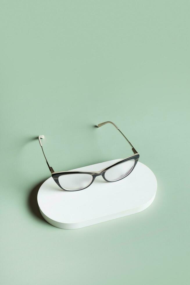 podium avec lunettes sur pastel vert Contexte. optique magasin, vision test, élégant des lunettes concept. photo