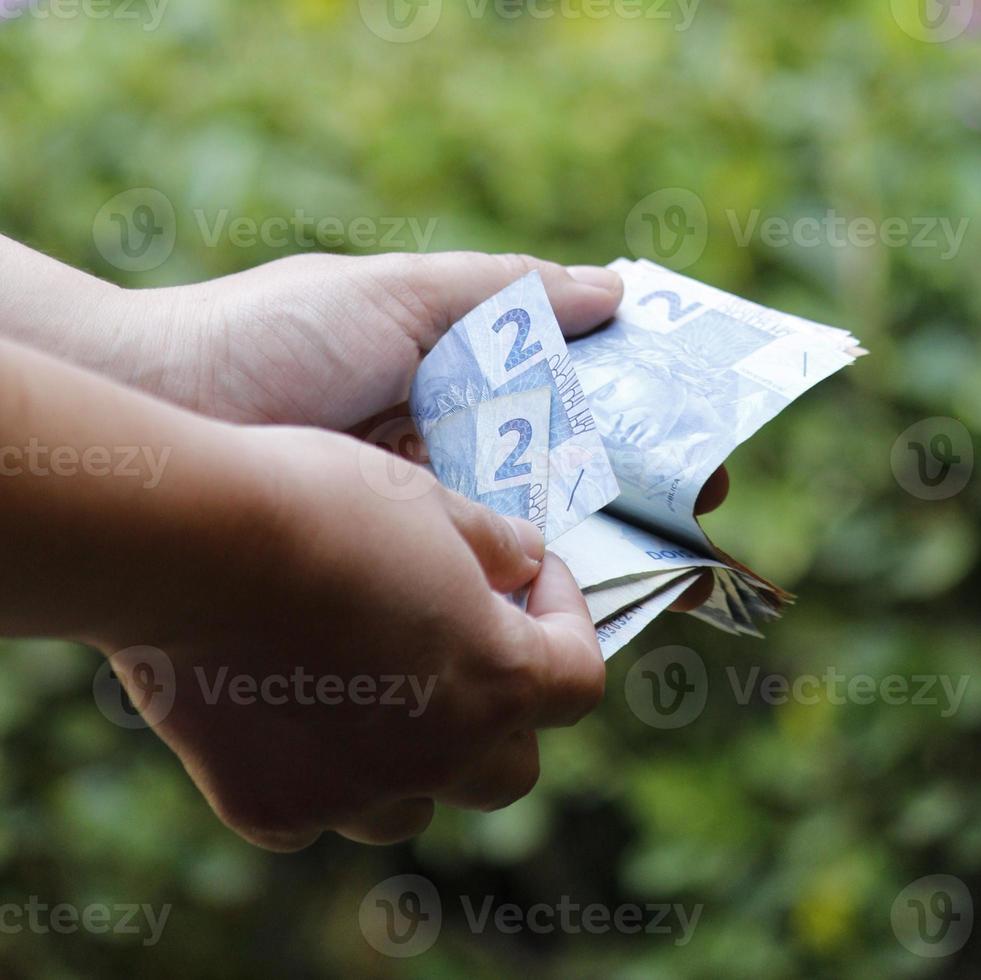 mains d'une femme comptant des billets de banque brésiliens dans un jardin photo