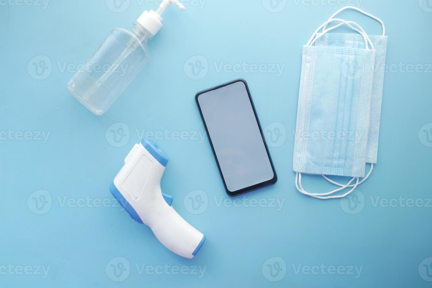 composition plate du téléphone intelligent, du masque, du thermomètre et du désinfectant sur la table photo