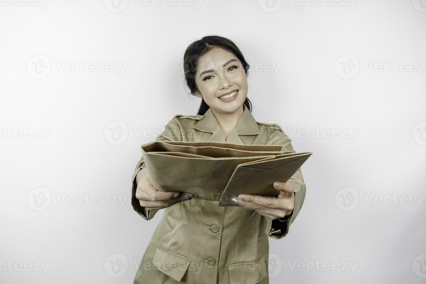 une Jeune magnifique asiatique ouvrier avec marron uniforme apportant document et remise il à le caméra. indonésien pns. photo
