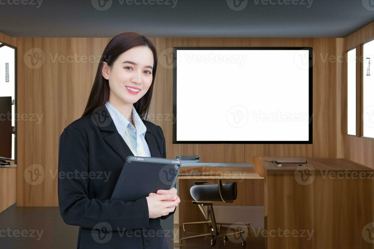 une jeune femme d'affaires professionnelle asiatique en costume noir sourit joyeusement avec confiance et regarde la caméra pendant qu'elle travaille et tient une tablette au bureau. photo