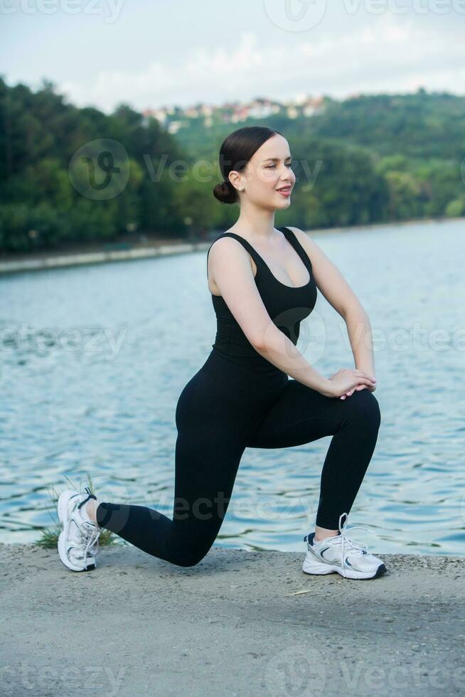 Jeune femme dans noir tenue de sport exercice en plein air. aptitude et en bonne santé mode de vie concept. le blanc fille Est-ce que des sports dans le parc. photo