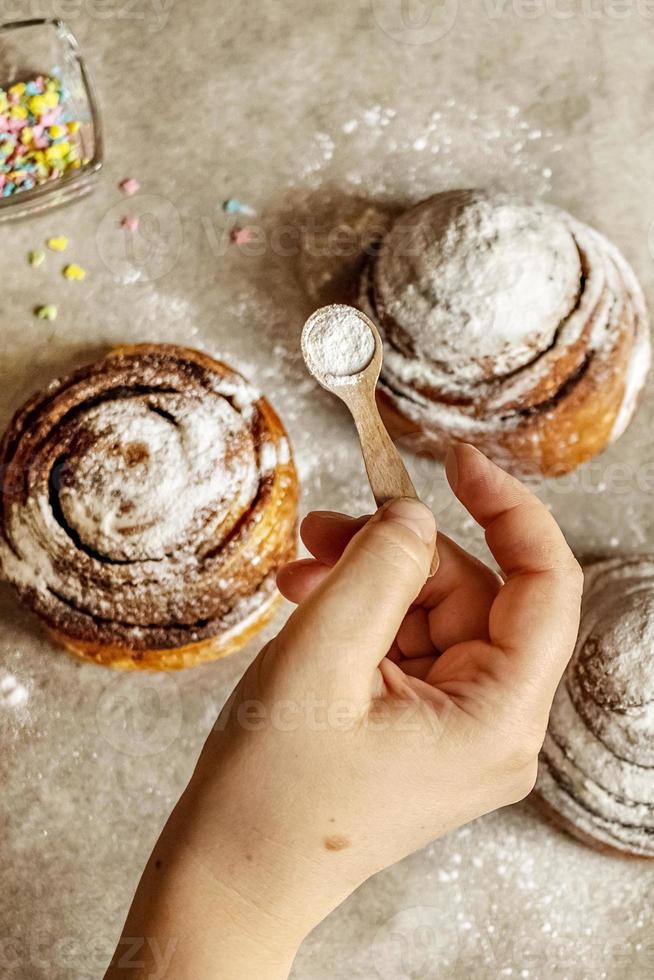 la main de la femme saupoudre de sucre glace sur des brioches à la cannelle fraîchement cuites photo