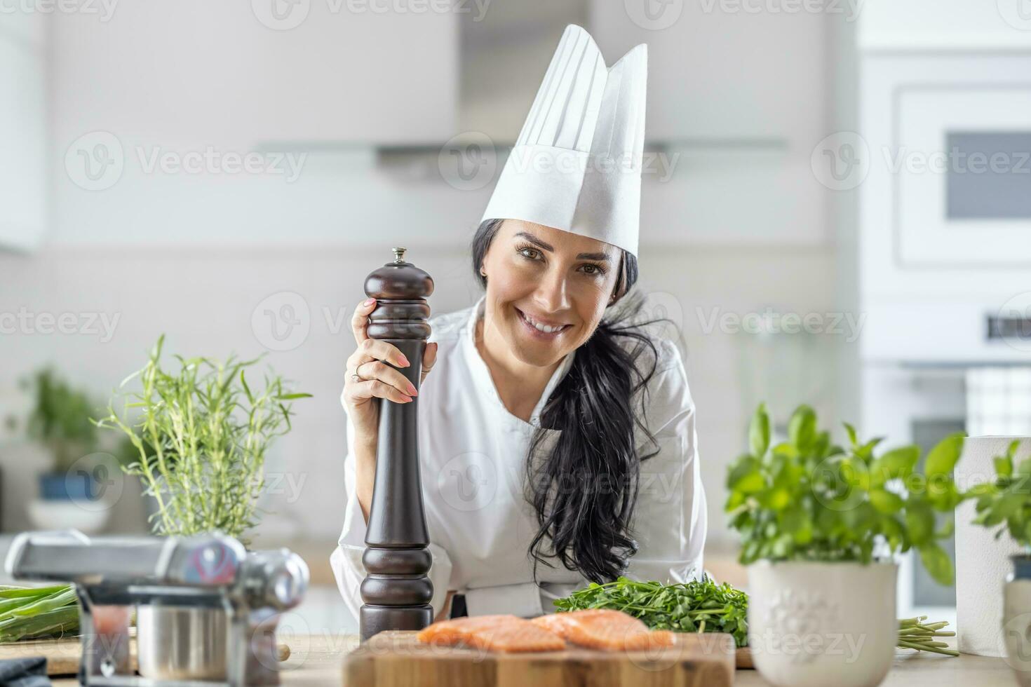 femelle chef dans toque blanche, blanc chapeau, et uniforme détient une poivre broyeur pendant poisson et veg repas préparation photo