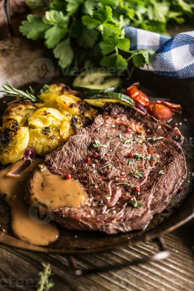 juteux du boeuf nervure œil steak rôti patates avec sauce grillé légume sel poivre et herbes dans ancien la poêle photo