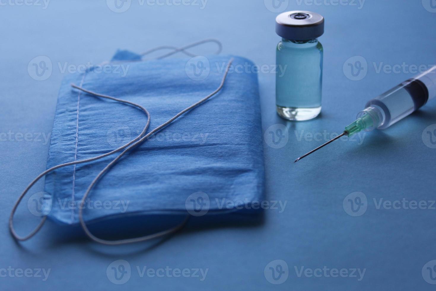 bouteille en verre avec médicament, seringue et masque jetable sur la surface bleue photo