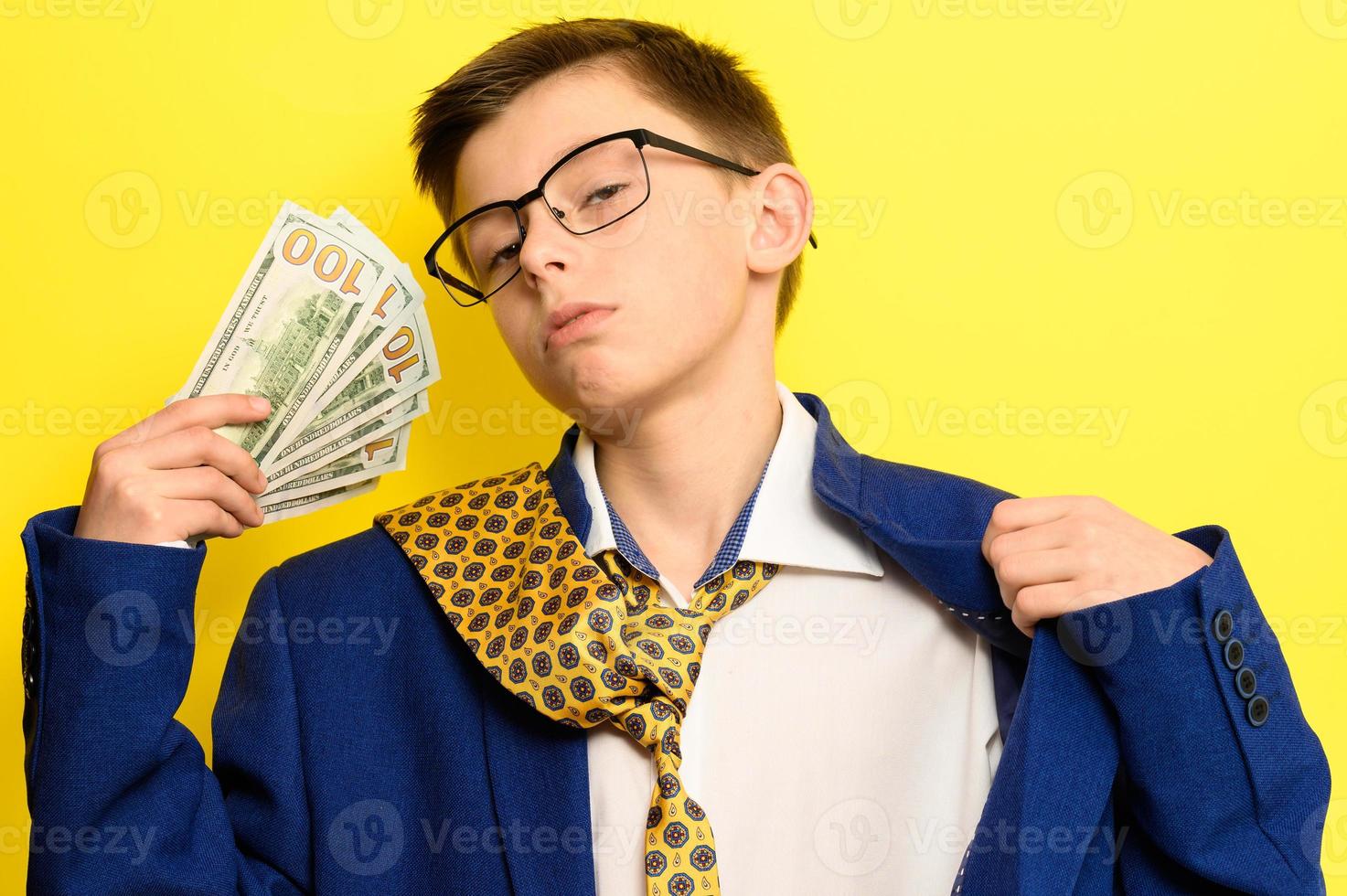 un gars dans un grand costume classique sur fond jaune tient une devise étrangère, un enfant à lunettes et un costume avec une cravate. photo