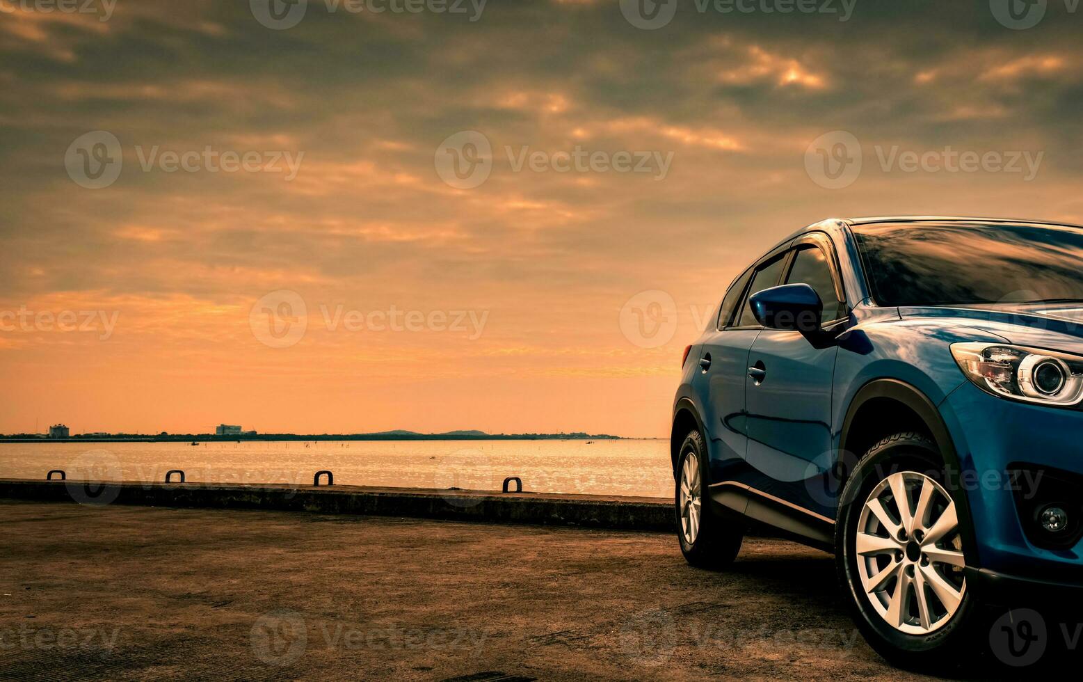 voiture suv compacte bleue au design sportif et moderne garée sur une route en béton au bord de la mer au coucher du soleil le soir. concept de technologie de voiture hybride et électrique. place de parking. industrie automobile. photo