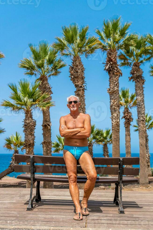 portrait de attrayant milieu vieilli homme portant maillot de bain avec canarien paume des arbres comme une Contexte photo