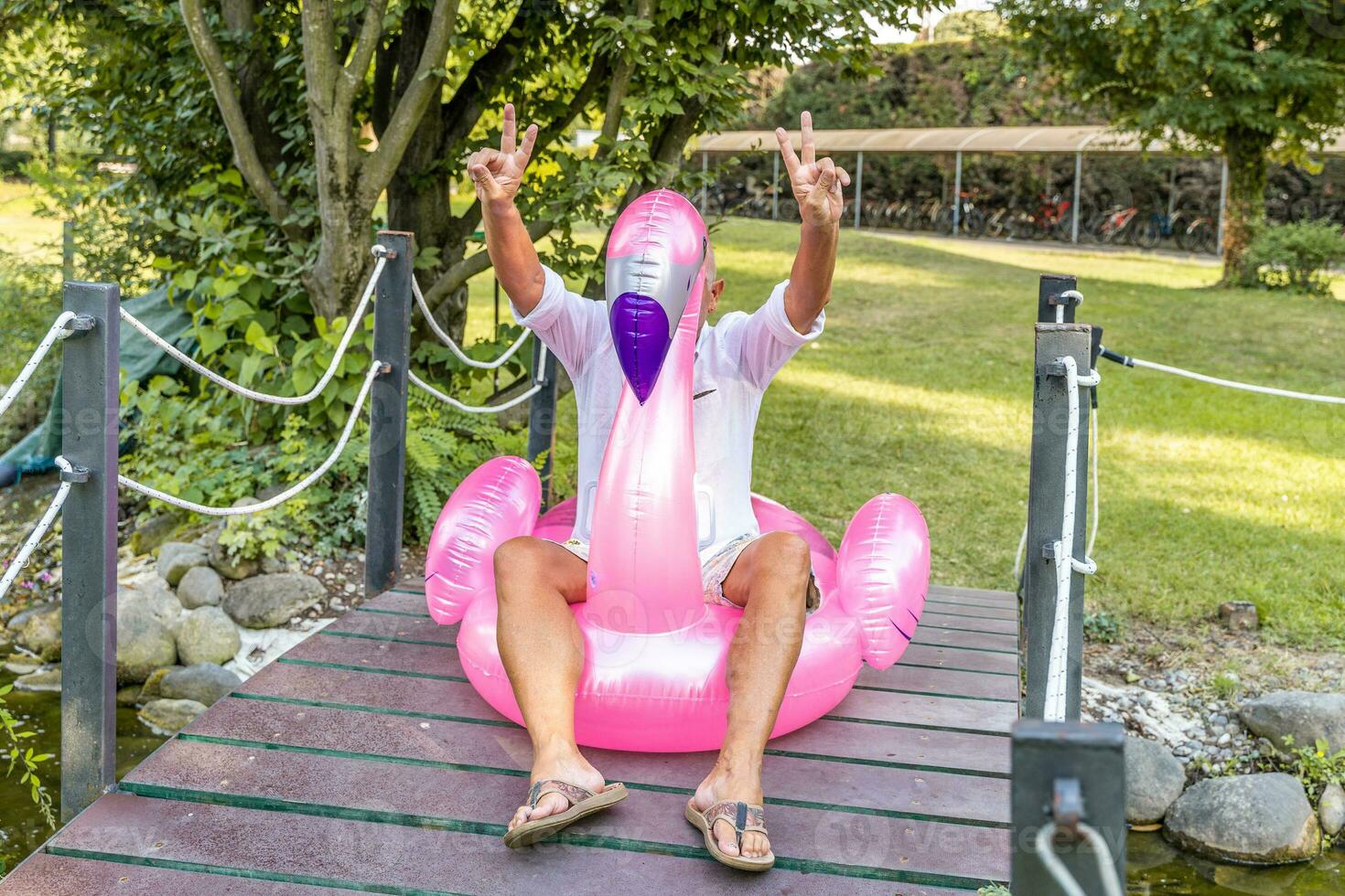 souriant Beau milieu vieilli homme ayant amusement séance sur un gonflable flamant jouet photo