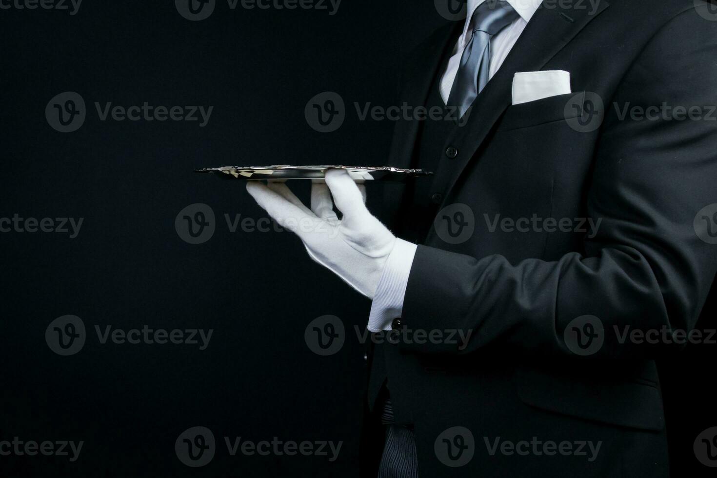 portrait de élégant majordome ou la conciergerie dans foncé costume et blanc gants en portant argent portion plateau. photo