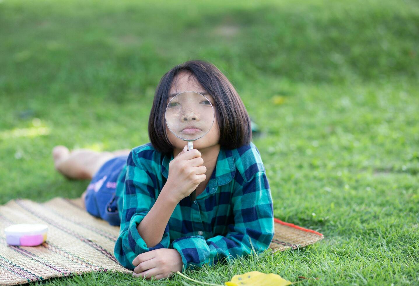 asiatique peu fille est en utilisant grossissant verre à jouer dans le parc.sstkhome photo