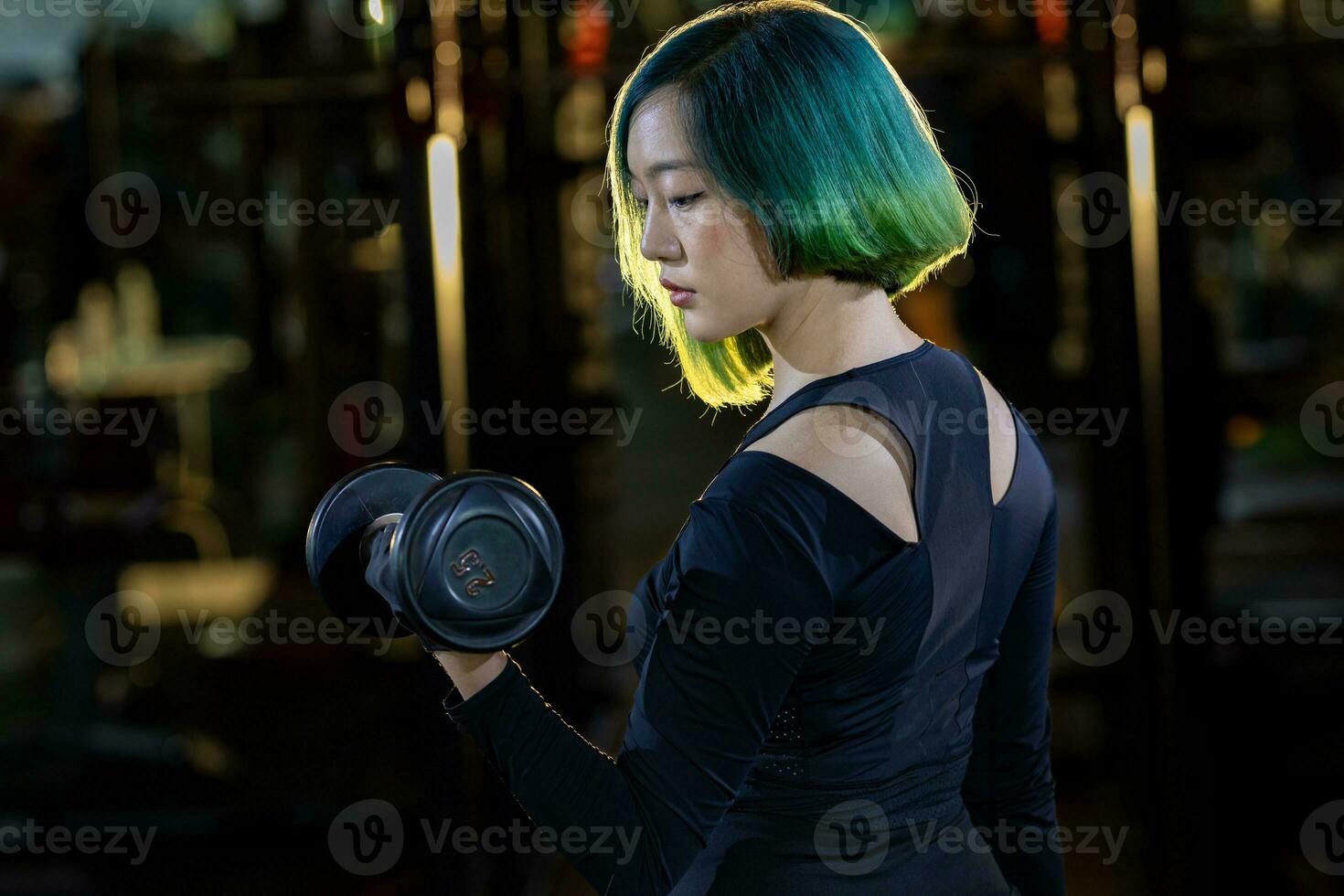 asiatique femme est entraine toi poids vivant comme débutant sur haltère pour bras et coeur muscle à l'intérieur Gym avec foncé Contexte pour exercice et faire des exercices photo