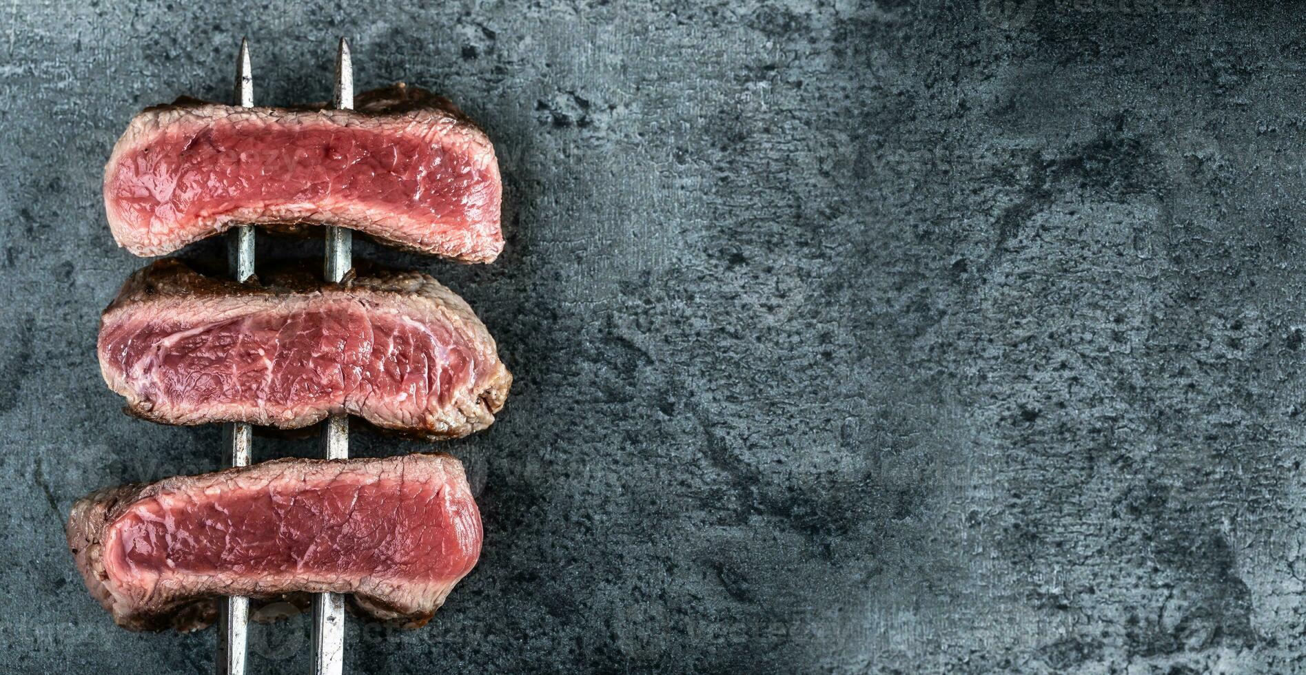 biaisé steaks de du boeuf cuit sur chaud foncé des pierres vu de le Haut photo