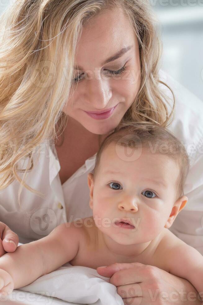 mère et bébé garçon fils en jouant sur une blanc lit. les mères tendresse et baisers de une bambin enfant photo