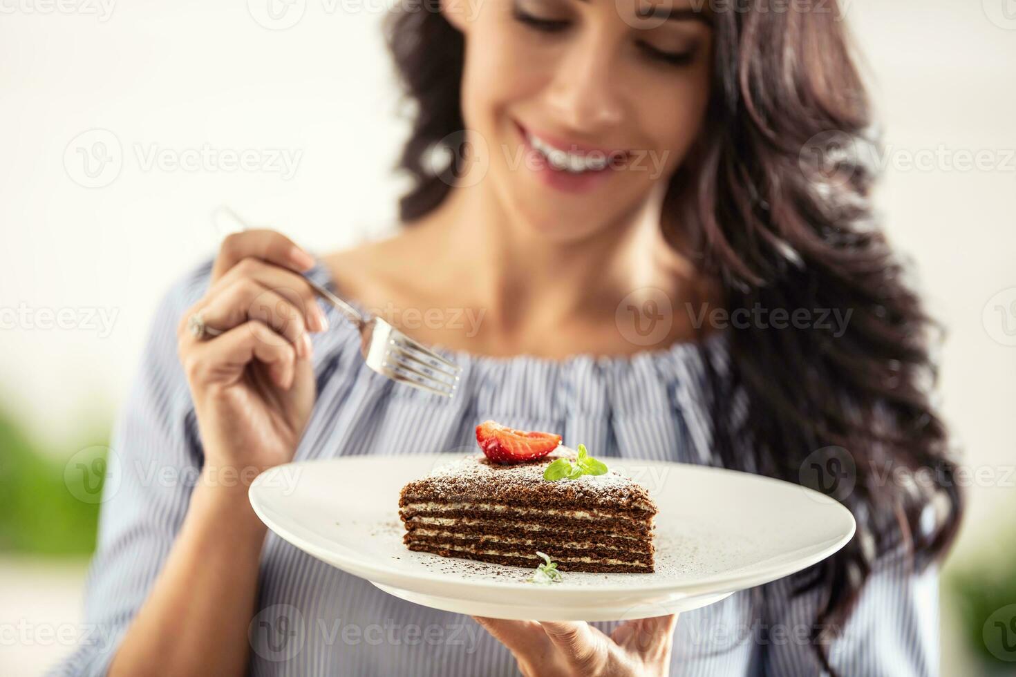 en couches marron adn blanc gâteau avec fraise et menthe feuille sur Haut tenue par une femme avec une fourchette photo