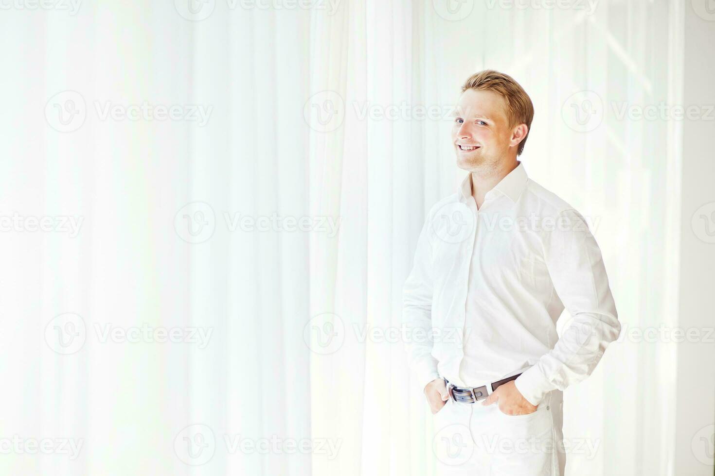 une homme dans une blanc chemise permanent dans de face de une fenêtre photo