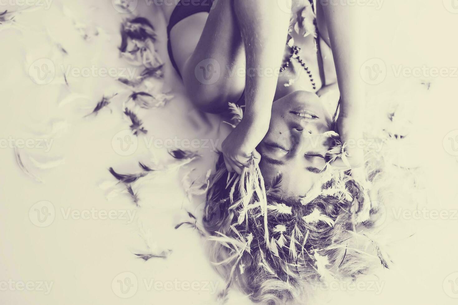 une femme pose sur une lit avec sa cheveux couvert dans plumes photo