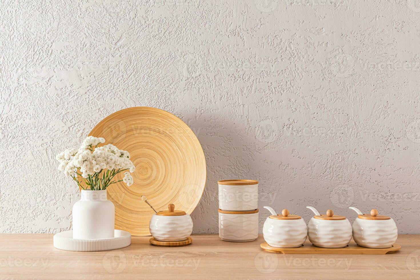 une ensemble de blanc céramique pots avec bambou couvercles pour stockage masse des produits et épices sur une en bois plan de travail avec blanc fleurs dans une vase. photo