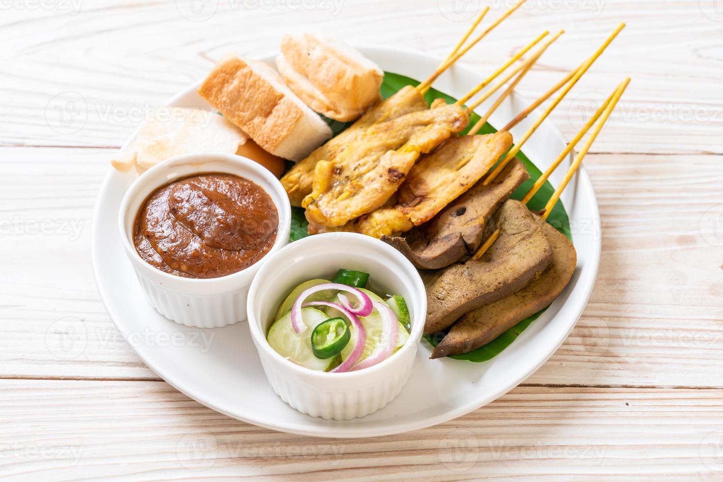 satay de porc avec votre sauce aux cacahuètes et cornichons qui sont des tranches de concombre et des oignons au vinaigre photo