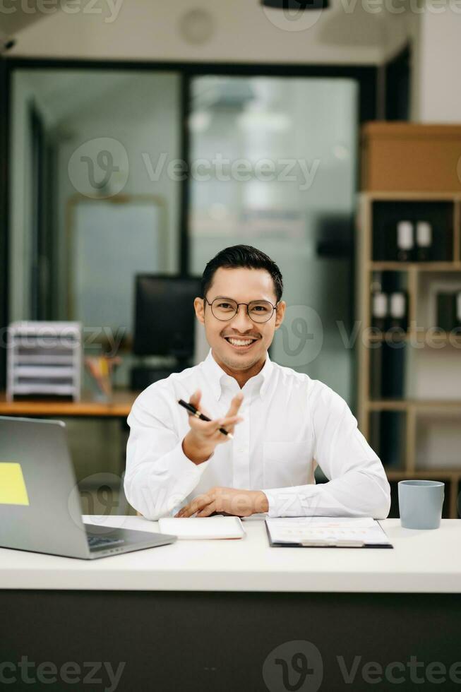 sur de soi asiatique homme avec une sourire permanent en portant bloc-notes et tablette à le bureau. photo