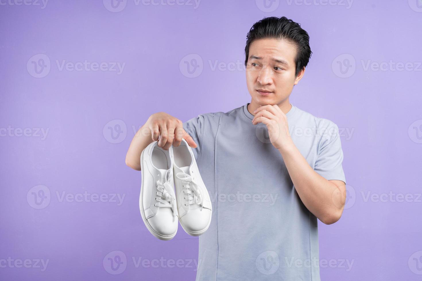 homme asiatique tenant des baskets sur fond violet photo