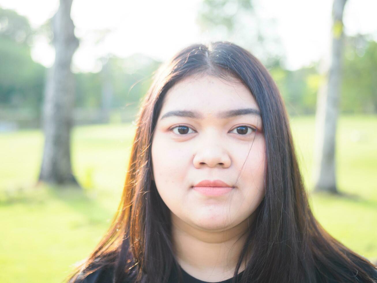 portrait Jeune femme fille asiatique joufflu mignonne magnifique longue noir cheveux un la personne porter noir chemise à la recherche dans jardin parc Extérieur soir lumière du soleil Frais souriant de bonne humeur content se détendre été journée photo