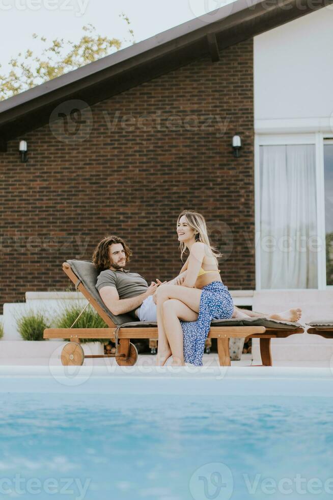 Jeune couple relaxant par le nager bassin dans le maison arrière-cour photo