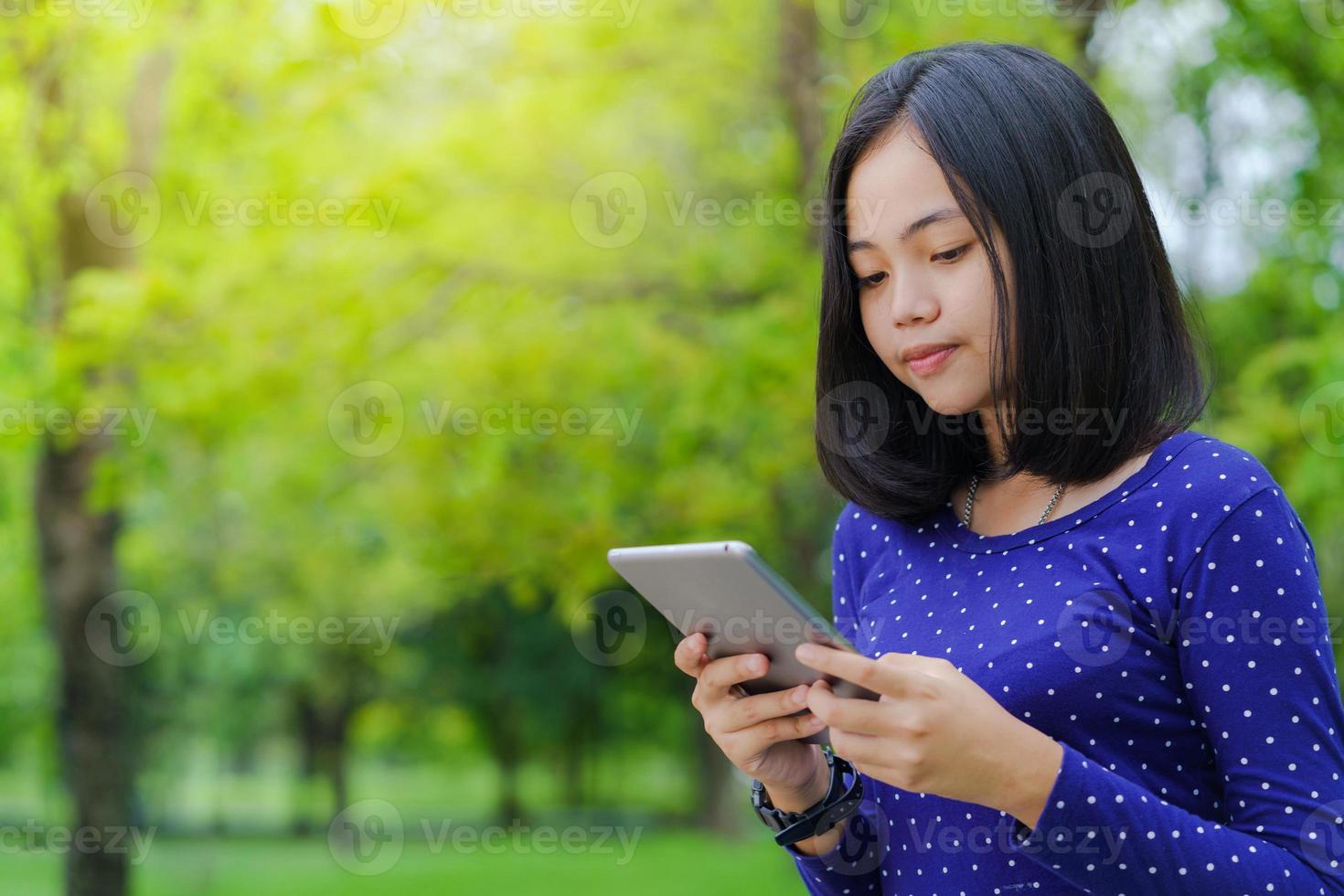 étudiante asiatique à l'aide d'une tablette numérique dans le parc par une journée d'été ensoleillée photo