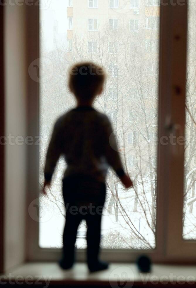 garçon est à la recherche par le la fenêtre. photo