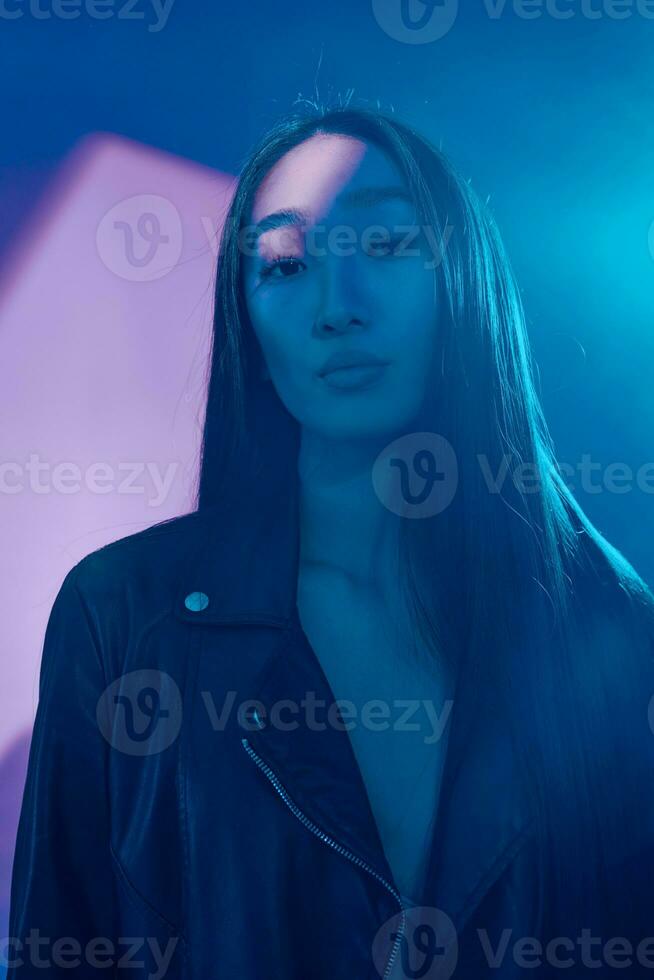 une femme dans une cuir veste permanent dans de face de une bleu lumière photo